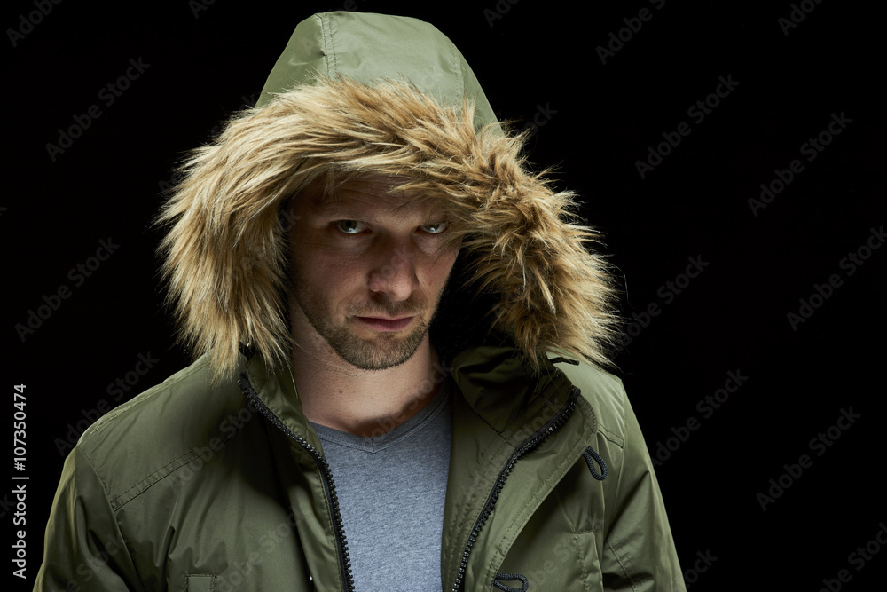 Low key studio portrait of suspicious young adult caucasian model wearing winter coat with hood on. Low key studio portrait of suspicious young adult caucasian model wearing winter coat with hood on.