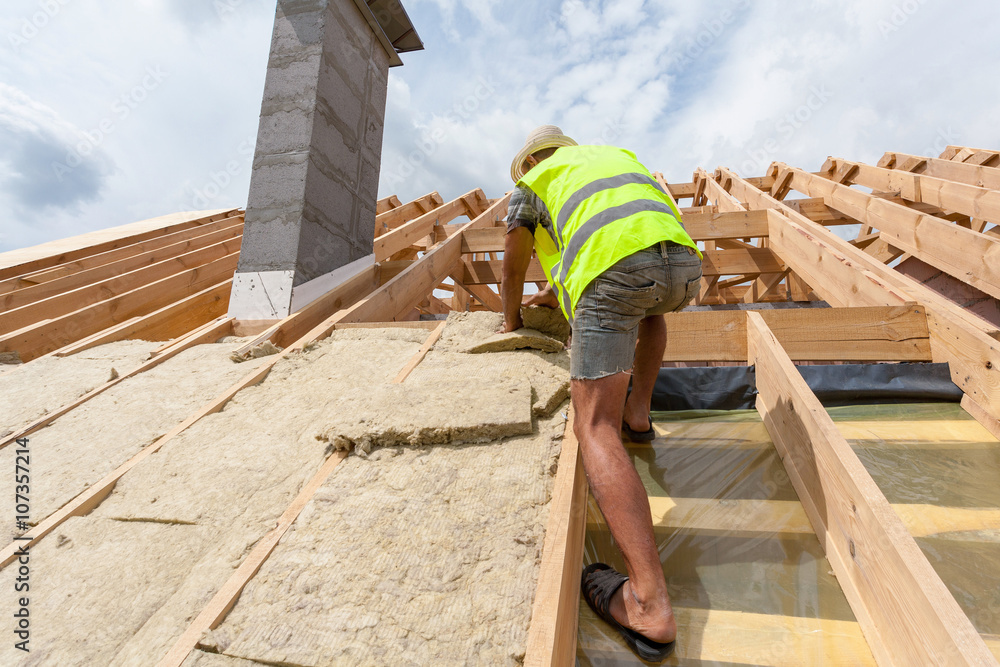 Roofer builder worker installing roof insulation material on new house under construction Roofer builder worker installing roof insulation material on new house under construction
