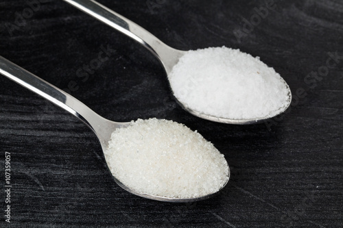 Spoon with salt and sugar on wooden table in kitchen