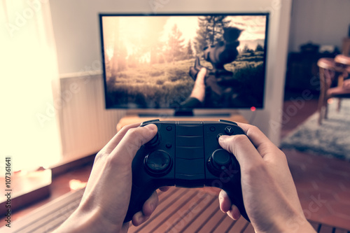 Playing game on console - hands holding game pad and playing shooter game on tv screen. photo