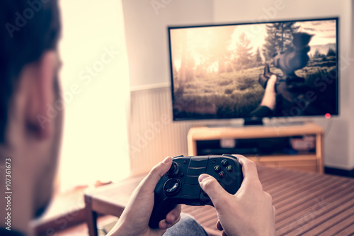 Playing game on console - hands holding game pad and playing shooter game on tv screen. photo