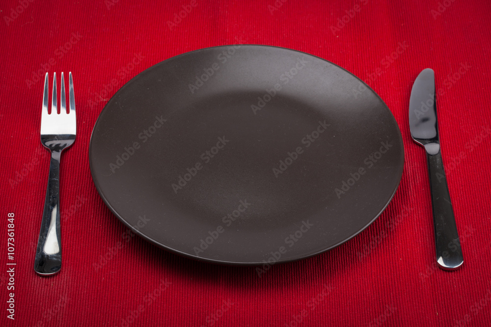 Empty plate with fork and knife on red tablecloth Empty plate with fork and knife on red tablecloth