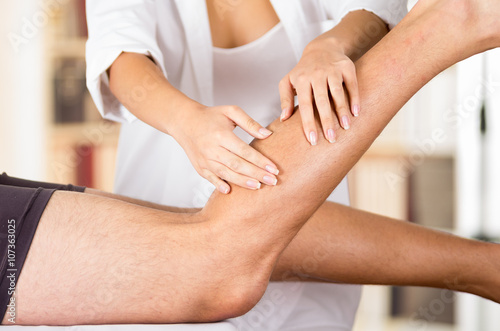 Closeup female physio therapist hands working on male patients legs, blurry clinic background