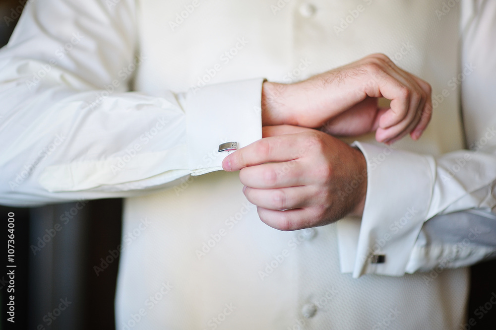 Fototapeta premium groom in morning on wedding day buttoning cuffs his hands