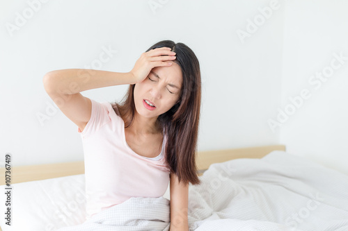 Woman feeling haedache and sitting on bed