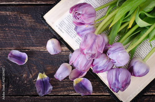 Fototapeta Naklejka Na Ścianę i Meble -  Violet tulips, petals, book on wooden background. Vintage and retro style.