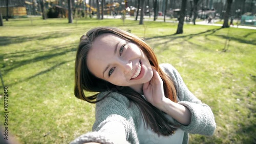 Portrait of a beautiful young woman selfie in the park with a smart phone. 