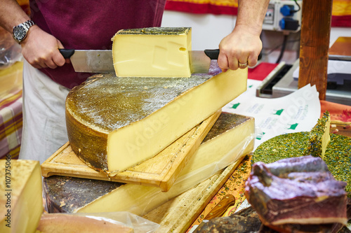 Man cutting slices of delicious cheese / Food market with abundance of high quality cheese