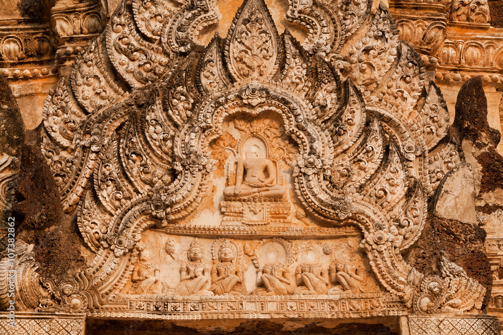 Floral patterns and Buddha figures on stone relief of ancient temple in Thailand