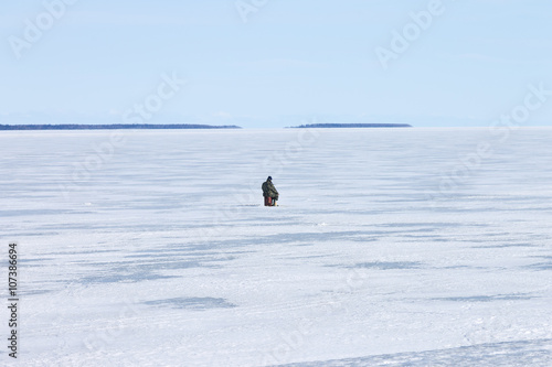 lonely fisherman on the frozen lake on a clear winter day fishing Ice hole