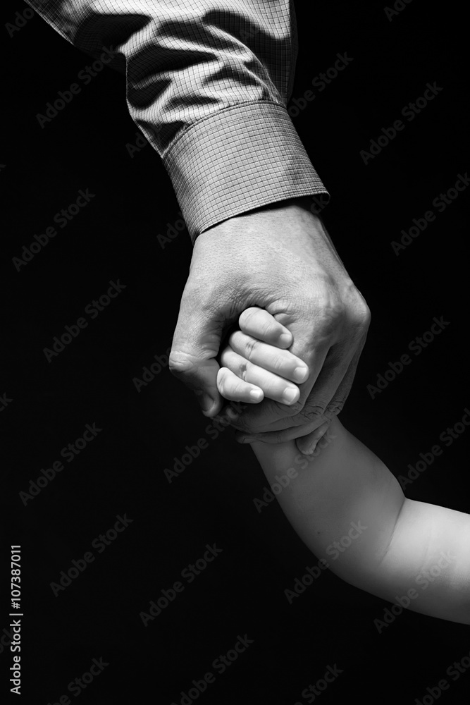 Father's hand holding child's hand. Hand businessman in shirt holding a child's hand. Isolated on black background. Grayscale.