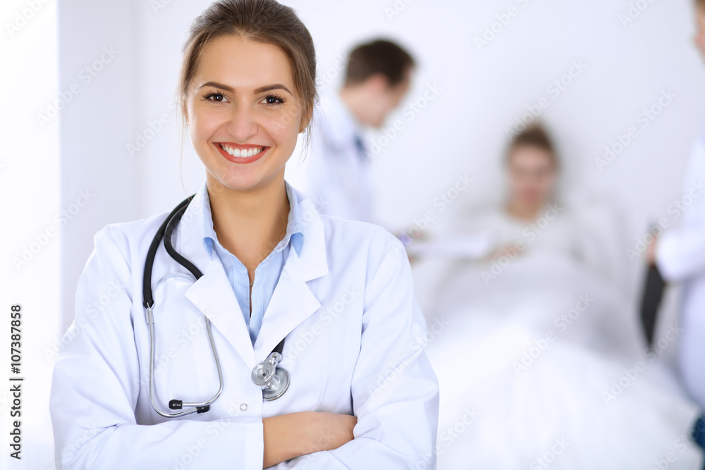 Female doctor smiling on the background with patient in the bed and two doctors Female doctor smiling on the background with patient in the bed and two doctors