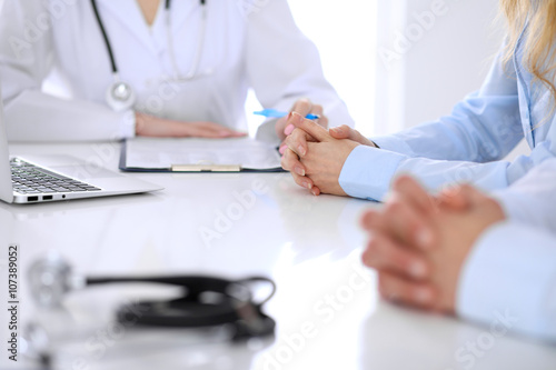 Medical doctor and young couple patients discussing something at the table . Hands close-up