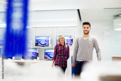 Couple in shopping at TV store. They are walking and holding big unpacked tv. Shallow depth of field. Selective focus on him.