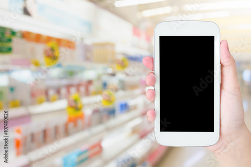 Female hand holding mobile phone on Supermarket blurred backgrou