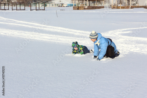 The woman and the little boy in a color jacket playing on snow in the winter