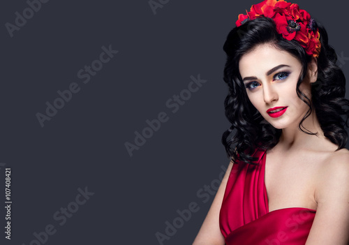 Lady in red. Beautiful woman portrait in red dress, with red lips and accessories. Young girl brunette with red flowers in hair. Bright makeup and nice hairstyle.