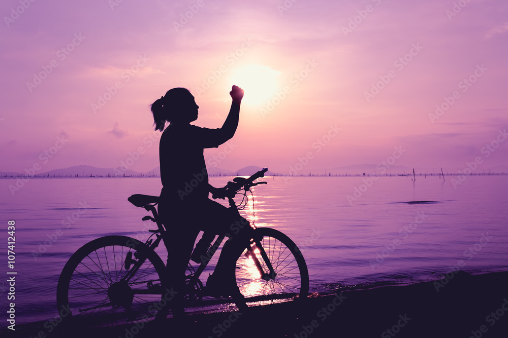 Fototapeta premium Silhouette of happy female celebrating with arm up towards the sun