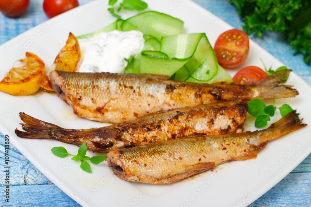 Roasted sardines with a salad of cucumber and yogurt on a wooden background. Mediterranean cuisine Roasted sardines with a salad of cucumber and yogurt on a wooden background. Mediterranean cuisine