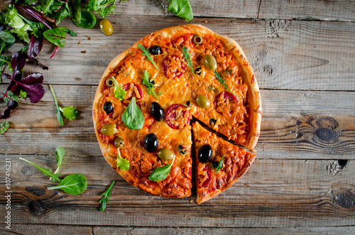 Rustic pizza with salami, olives and fresh herbs top view
