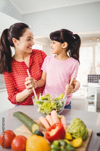 Happy mother and daughter preparing salad