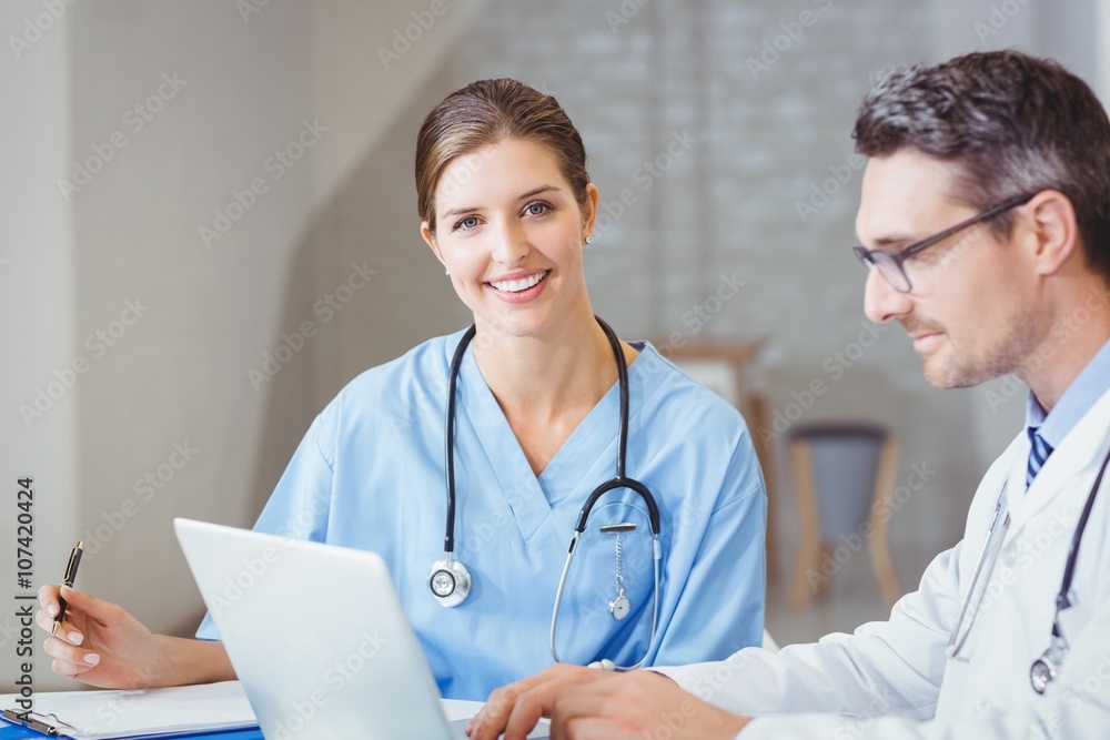 Portrait of smiling doctor sitting at desk with colleague Portrait of smiling doctor sitting at desk with colleague