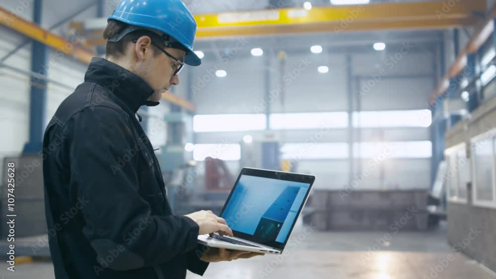Factory worker in a hard hat is using a laptop computer with an engineering software. Shot on RED Cinema Camera. Factory worker in a hard hat is using a laptop computer with an engineering software. Shot on RED Cinema Camera.