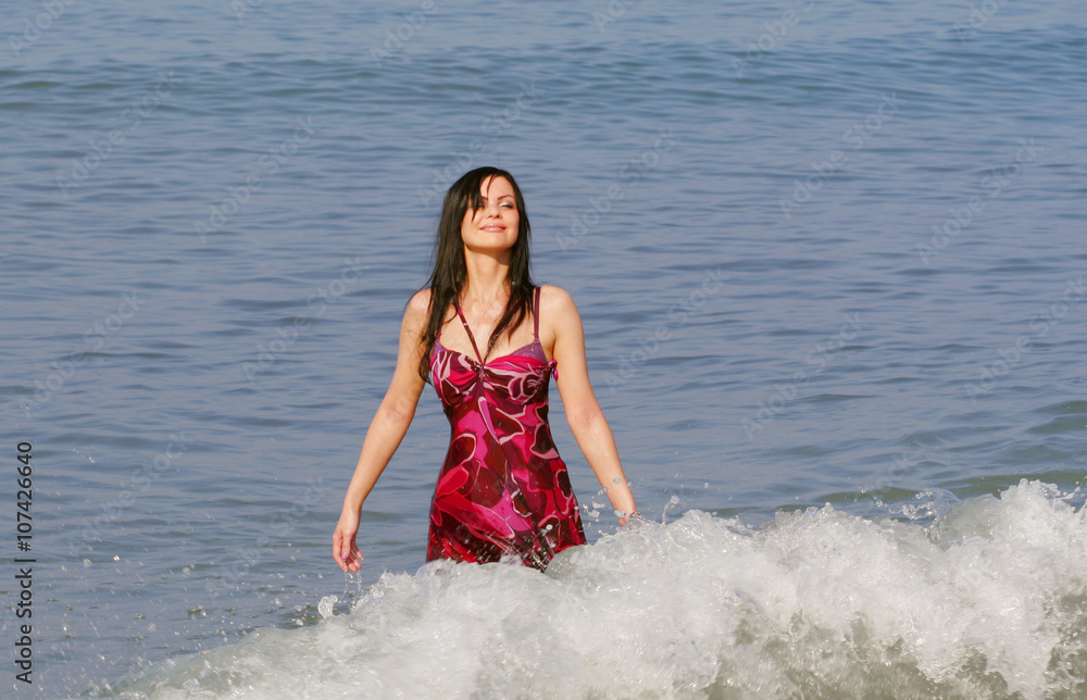 Fototapeta premium Young smiling woman standing in sea waves