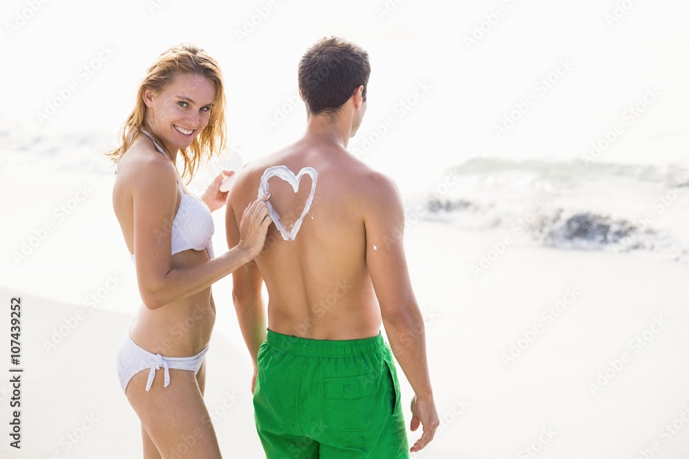 Woman making a heart symbol on mans back while applying a sunscreen lotion at beach Woman making a heart symbol on mans back while applying a sunscreen lotion at beach