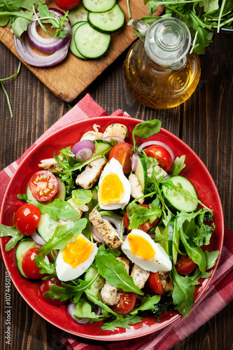 Fresh salad with chicken, tomatoes, eggs and arugula on plate