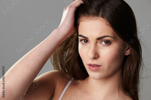 Dark haired, late teen girl touching hair looking to camera