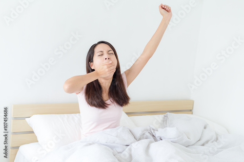 Woman yawning and sitting on bed