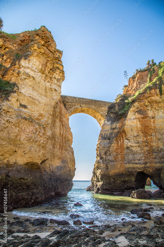 alte Steinbrücke zwischen zwei schroffen, gelben Klippen an der Algarve