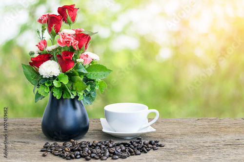Vase of roses and coffee cup on wooden floor with beautiful nature background.