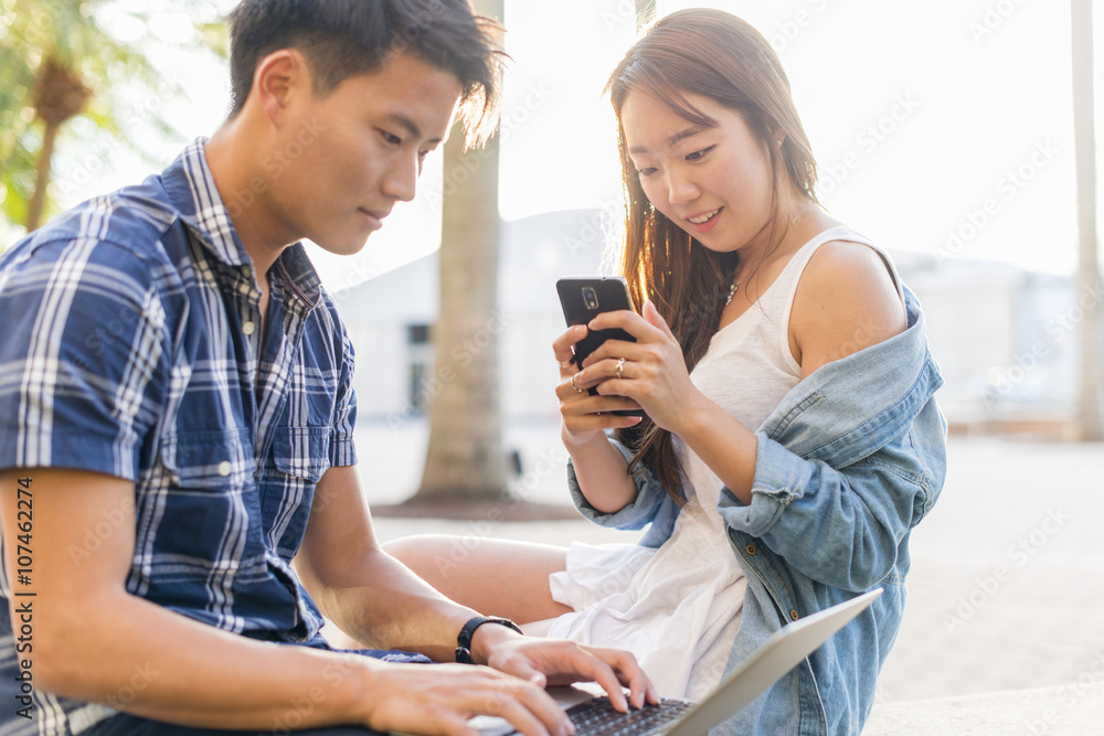 Korean couple using laptop and cell phone outdoors Korean couple using laptop and cell phone outdoors