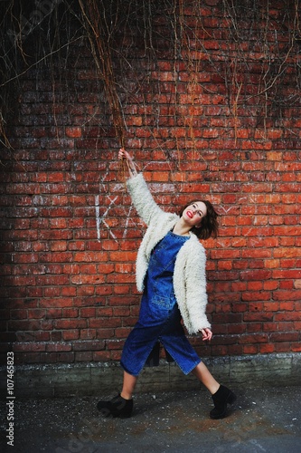 joyful girl grabbed hold of the branches hanging down near a brick wall.