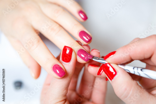 Manicure in progress - Beautiful manicured woman's nails with red nail polish. The industry of beauty and nail care, beauty salons, soft focus