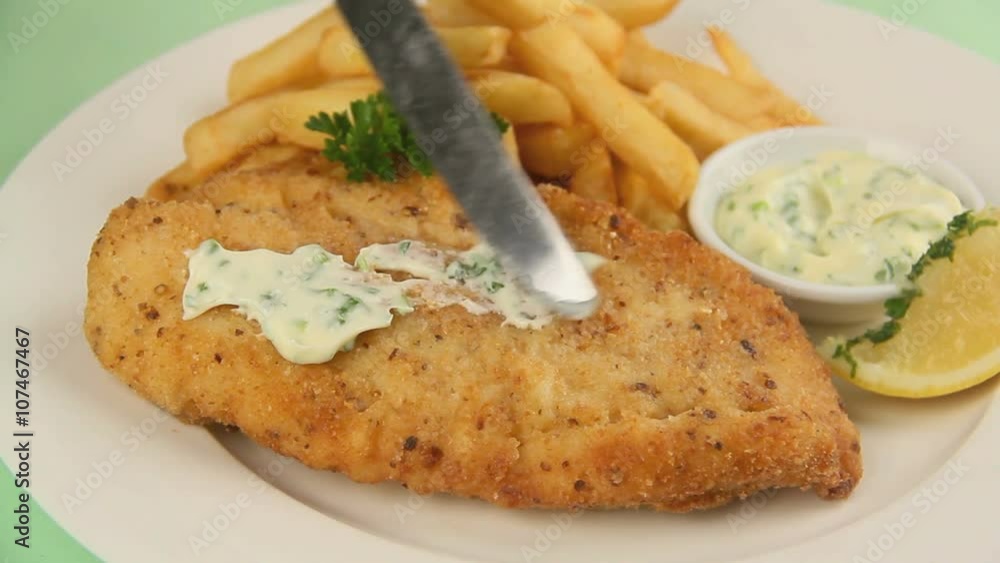 Spreading tartare sauce over a breadcrumbed fish fillet garnished with parsley. Spreading tartare sauce over a breadcrumbed fish fillet garnished with parsley.