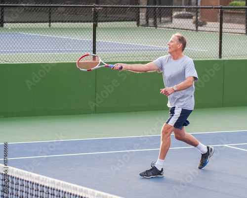 Senior age man showing perfect follow through on running volley. 