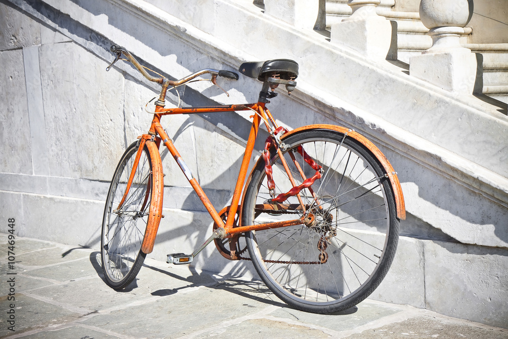 Old rusty orange bicycle against a marble wall (Tuscany - Italy)