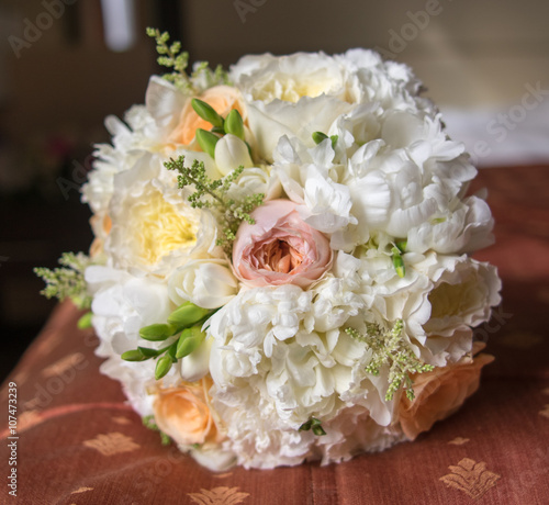 White bouquet of the bride with freesia, roses and peonies, lying on the bed