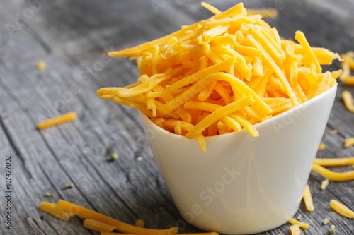 Shredded cheddar cheese in white cup close up view