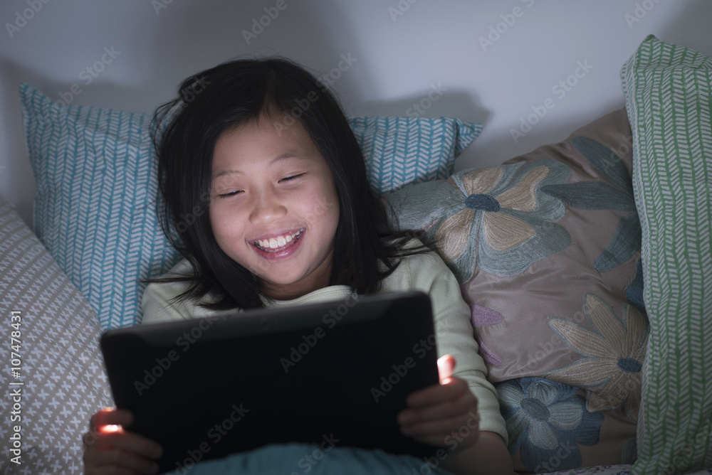 Smiling Chinese girl watching digital tablet in bed Smiling Chinese girl watching digital tablet in bed