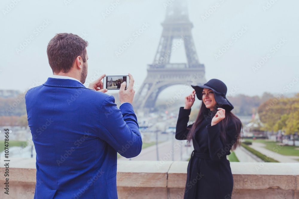 Obraz premium mobile photography, man taking photo of woman with his phone, couple of tourists near Eiffel Tower in Paris, France