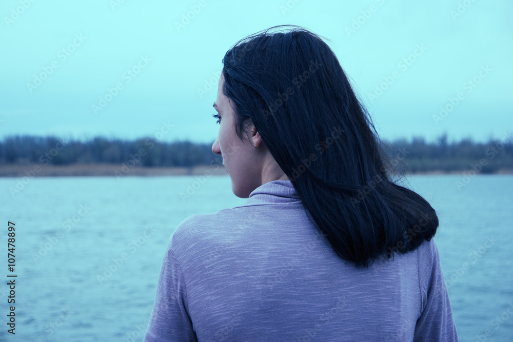 Beautiful young woman is looking at view over the river.Attractive woman enjoys summer rear view.
She is admiring beautiful view and enjoying soft sunlight.Instagram-like color filter. Vintage color