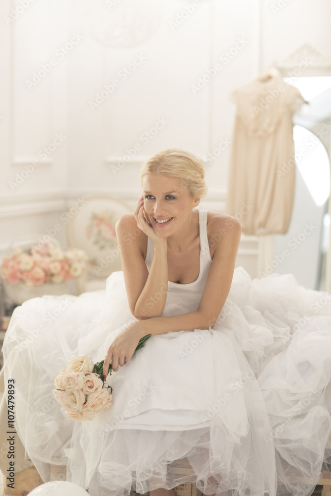 Smiling bride sitting with bouquet on bed Smiling bride sitting with bouquet on bed