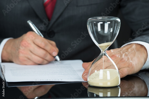 Close-up Of Businessman Filling Form With Hourglass