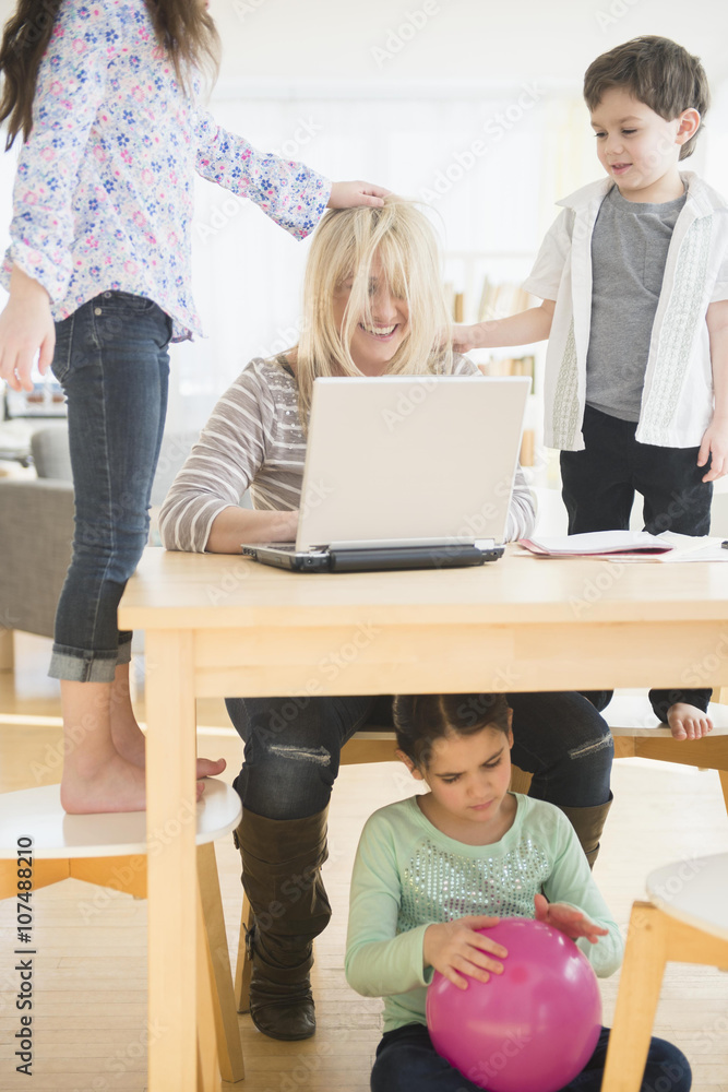 Caucasian mother using laptop with chaotic children Caucasian mother using laptop with chaotic children