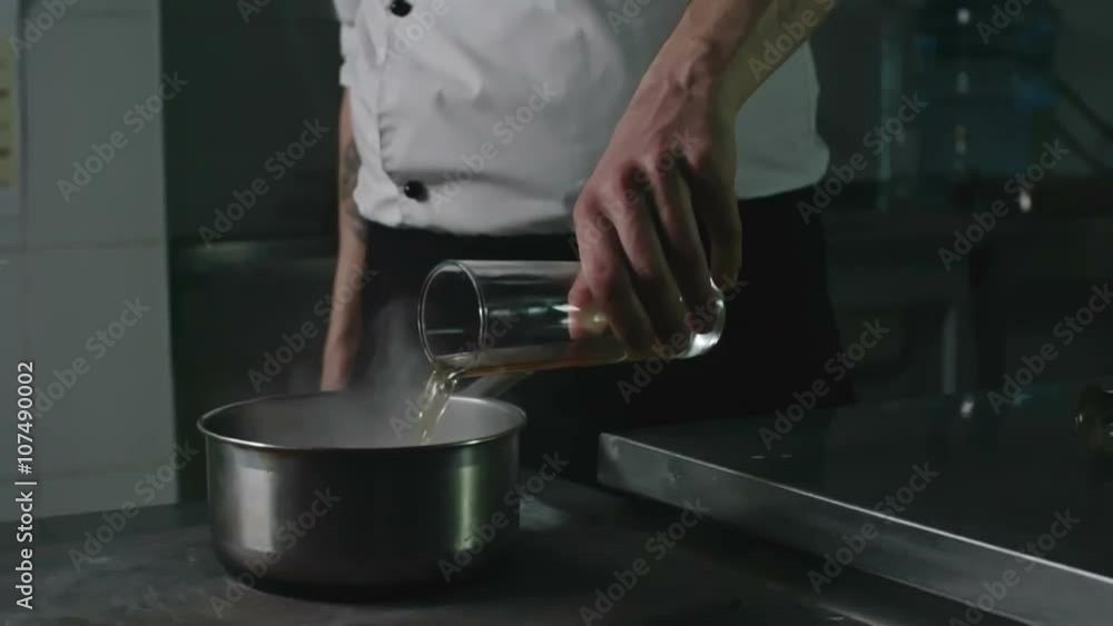 Close up of restaurant chef adding alcohol to a hot saucepan and creating a burst of flame in it to make a flambe dish Close up of restaurant chef adding alcohol to a hot saucepan and creating a burst of flame in it to make a flambe dish
