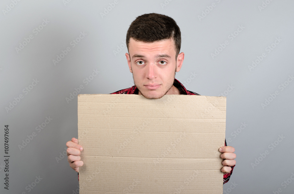 Portrait of young man showing blank signboard, with copyspace area for text or slogan, against grey background Portrait of young man showing blank signboard, with copyspace area for text or slogan, against grey background